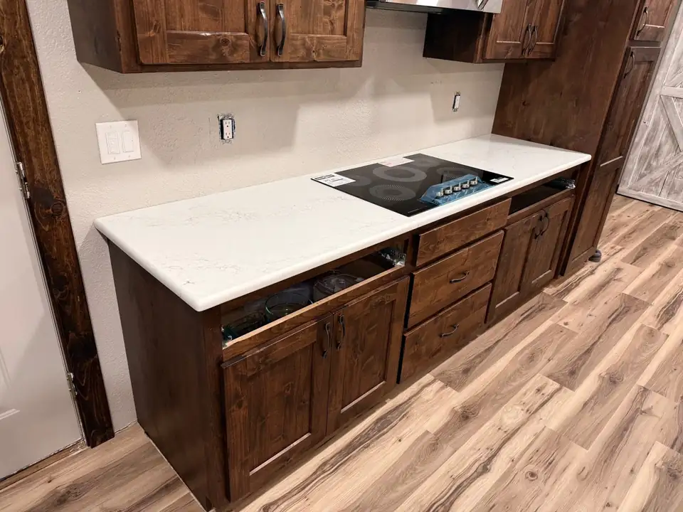 Countertops in Enid from The Countertop Shop: white countertop on dark rustic cabinets with a black cooktop and wood-look floor
