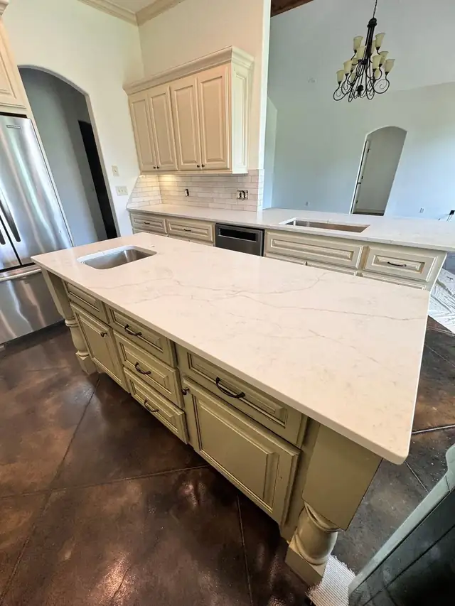 White veined countertop on a cream painted island with an undermount sink and turned legs