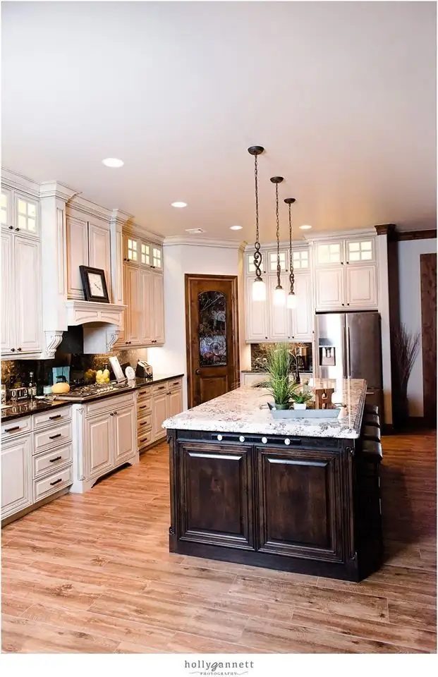 White kitchen with a dark wood island, light stone counters and three pendant lights