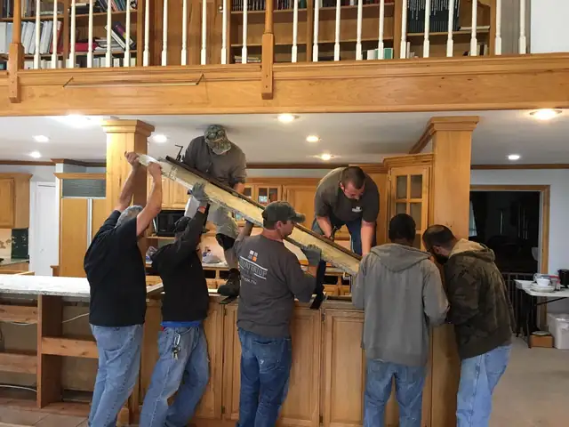 Countertop Shop crew of five lifting a heavy granite slab into place on a kitchen bar