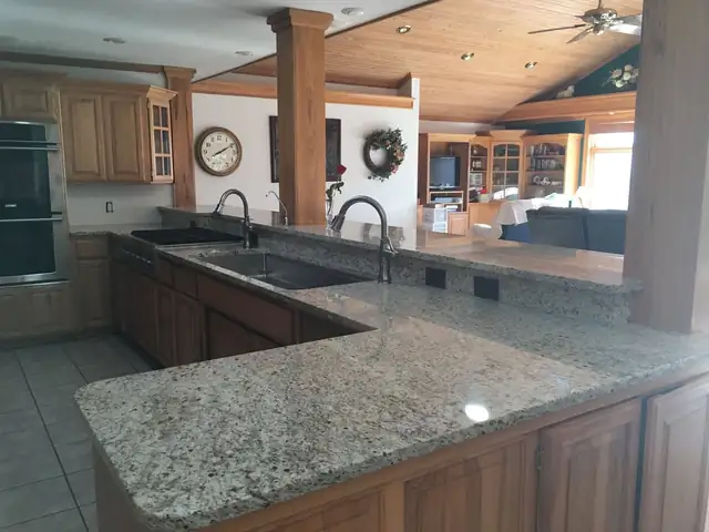 Granite countertops and bar on honey oak cabinets, fitted around wood posts in an open kitchen
