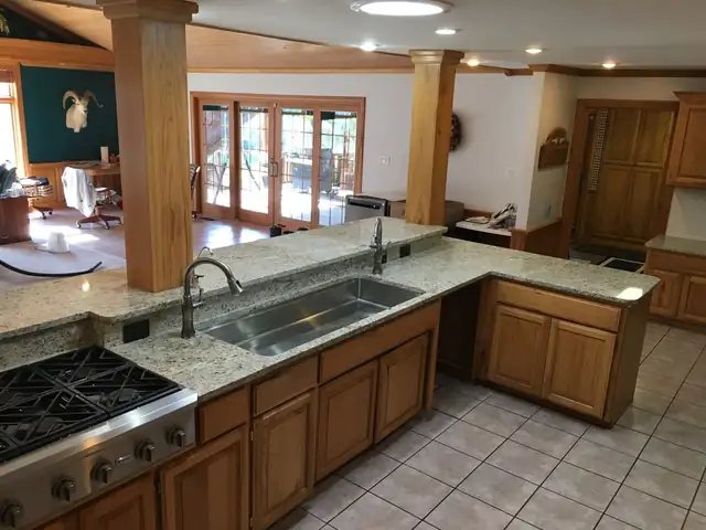 Granite countertops with an undermount sink and a gas cooktop on wood cabinets beside timber posts