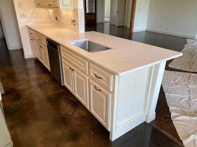 White cabinet island with a light countertop and undermount sink on a stained concrete floor